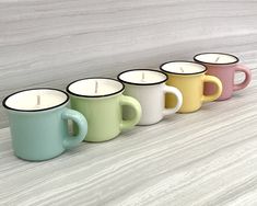 five different colored coffee mugs lined up in a row with one candle on the side