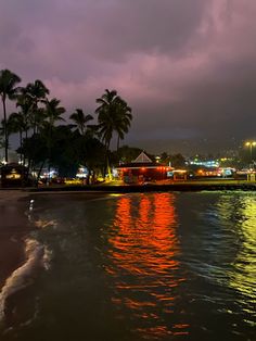 the beach is lit up at night with palm trees in the foreground and buildings on the other side