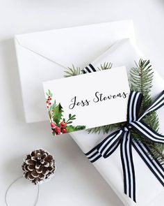 a christmas present wrapped in white paper with a black ribbon and pine cone on top