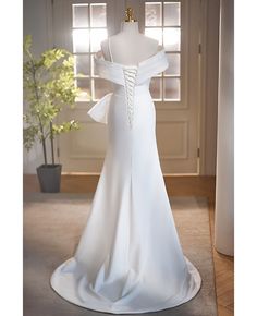 a white wedding dress on display in front of a window with a potted plant