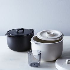 two pots and one glass are sitting on the table next to each other, both with lids