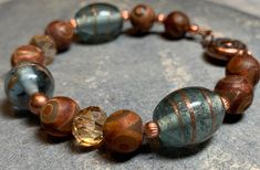 a close up of a bracelet with beads on a stone surface and one bead