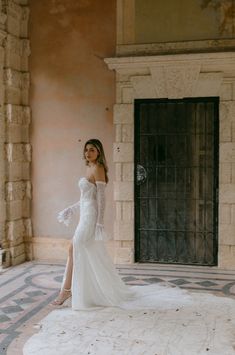 a woman in a white wedding dress standing on a stone floor with her legs crossed