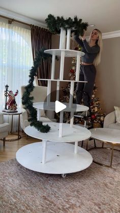 a woman standing on top of a white shelf next to a christmas tree in a living room