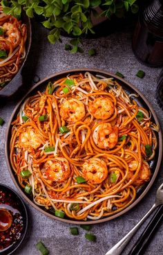 a plate full of noodles with shrimp and sauce on the side next to some chopsticks