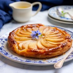 a blue and white plate topped with a pastry covered in apple slices next to a cup of tea