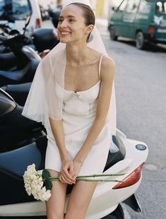 a woman sitting on the back of a scooter wearing a white wedding dress