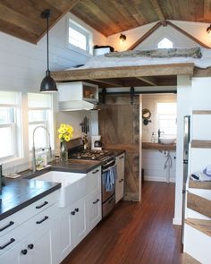 a kitchen with white cabinets and wood floors in a loft style home that has stairs leading up to the ceiling