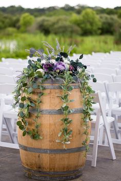 a wooden barrel with flowers and greenery on the top sits in front of rows of white chairs