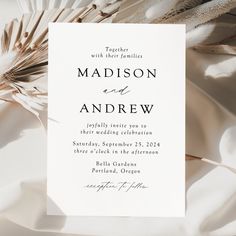 the wedding card is laying on top of some white fabric with feathers attached to it