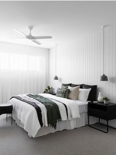 a bedroom with white walls, black and green bedding and two lamps on either side of the bed