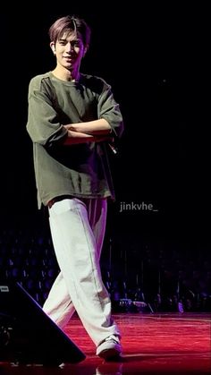 a young man standing on top of a stage with his arms crossed and legs crossed