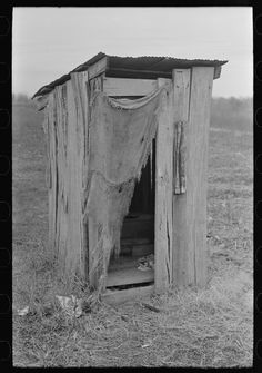 an outhouse in the middle of a field with clothes hanging from it's roof