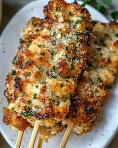 two chicken skewers on a white plate with parmesan cheese and herbs