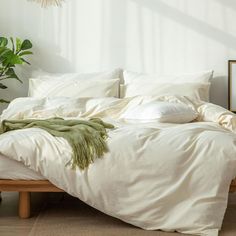 an unmade bed with white linens and green throw pillows in a neutral bedroom