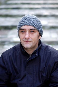 a man wearing a knitted hat looks at the camera while standing in front of some steps