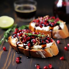 two pieces of bread topped with pomegranate and cream cheese on a wooden table