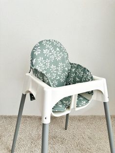 a white high chair with green and white patterned seat covers on it's legs