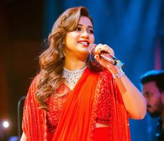 a woman in an orange sari singing into a microphone