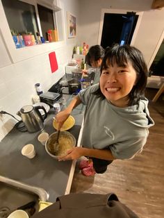 a woman standing in front of a kitchen counter holding a bowl with food on it