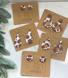 four brown and white cow earrings sitting on top of a table next to a plant