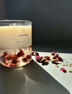 a candle that is sitting on a table next to some dried rose petals and leaves