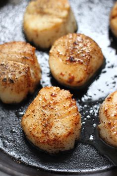 seared scallops cooking in a skillet with oil on them and seasoning sprinkles