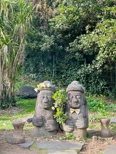 two stone statues sitting next to each other on top of a lush green park area