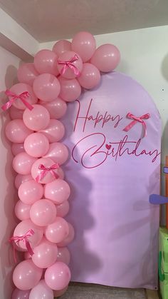 a birthday arch with balloons and streamers for the entrance to a room that is decorated in pastel colors