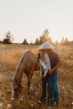 a man and woman standing next to a brown horse on a dry grass covered field