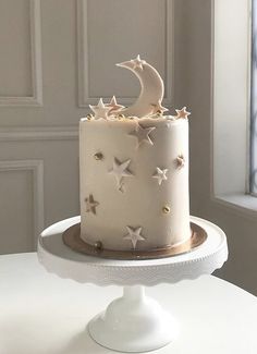 a white cake with stars and a moon on top is sitting on a table in front of a window