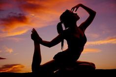 a woman sitting on the ground in front of a purple and orange sky at sunset