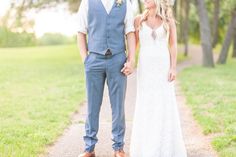 a bride and groom holding hands while standing on a path in the grass near trees