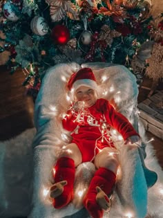 a baby in a santa outfit is sitting on a chair with christmas lights around it