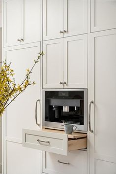 a kitchen with white cabinets and drawers has a coffee maker on the counter in front of it