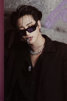 a woman wearing sunglasses and piercings poses for a photo in front of a wall