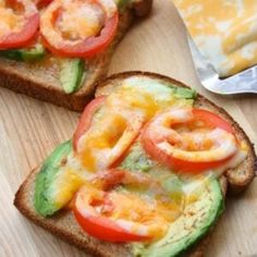 two slices of bread with tomatoes, avocado and cheese on them sitting on a cutting board