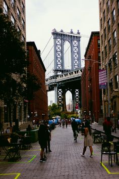 people are walking on the sidewalk in front of some tall buildings and a large bridge