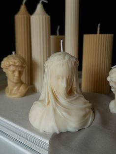 some candles are sitting on a table with statues in front of them and one candle has a woman's head