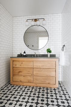 a bathroom with black and white flooring and a large round mirror above the sink