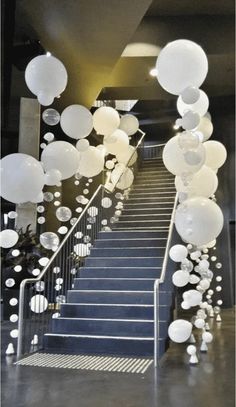 some white balloons are hanging from the ceiling and stairs in front of a staircase with blue carpet