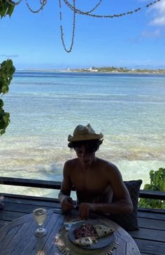 a shirtless man sitting at a table with food and drinks in front of him