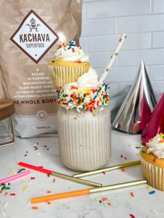 two cupcakes with white frosting and sprinkles in front of a bag of kachava coffee