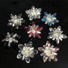 six crystal flower brooches on a black surface, each with different colors and sizes