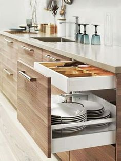 an open drawer in the middle of a kitchen counter with plates and glasses on it