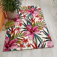 a white rug with pink flowers on it next to a potted plant and books