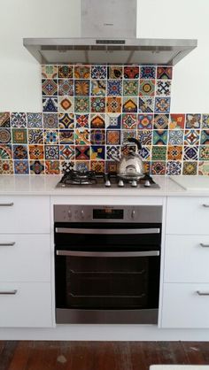 a stove top oven sitting inside of a kitchen next to a wall covered in colorful tiles