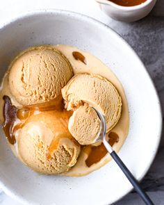 two scoops of ice cream in a bowl with caramel sauce on the side