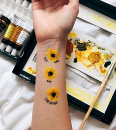 a woman's arm with sunflowers painted on it and some paint brushes