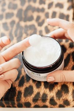 two hands holding a jar of cream on top of a leopard print table